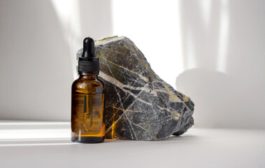 Mock-up of bottle with dropper lid, made of brown glass, against background of natural stone made...