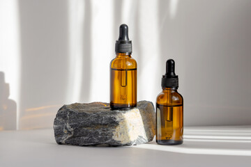 Two mockups of glass bottles with dropper lids on stand made of natural stone. Rays of sunlight...