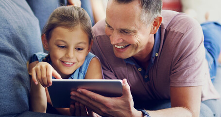 Modern day family time. Shot of a cute little girl using a digital tablet with her father on the sofa at home.
