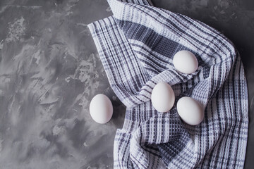 White chicken eggs lie on a white and blue napkin. Gray background. Easter preparations. Place for text, space.