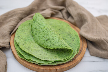 Delicious spinach crepes green colored pancake with vegetables on a table