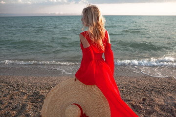 Beautiful strong woman wearing maxi straw hat and red chiffon cape like dresss walking in the beach...