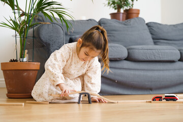 Toddler girl in white dress plays with wooden train at home in the living room 