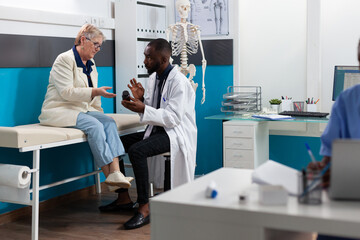 Obraz premium African american therapist doctor discussing sickness symptoms holding pills bottle explaining healthcare treatment to senior woman patient. Medical examination in hospital office. Medicine concept