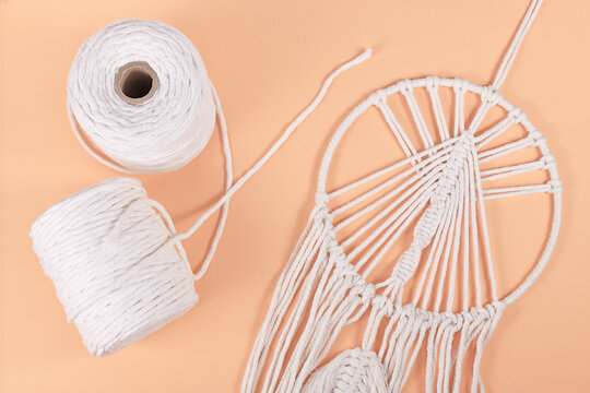Rolls of cotton macrame cord and finished wall hanging object on beige background