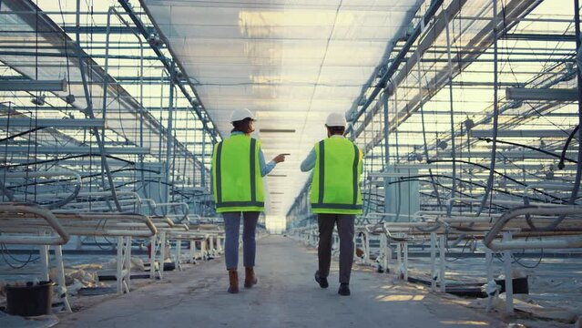 Two factory employees walking in empty greenhouse discussing production level