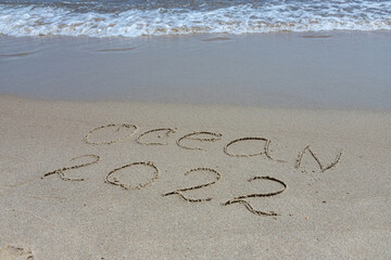 The inscription ocean 2022 on the sand by the water and the rising wave, seashore beach vacation by the sea