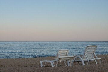 Two sunbeds on a sandy calm beach with turquoise sea water and white sand
