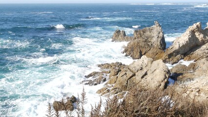 Rocky craggy ocean beach. Big waves crashing on bare cliff, blue water splashing, sea foam. Power...
