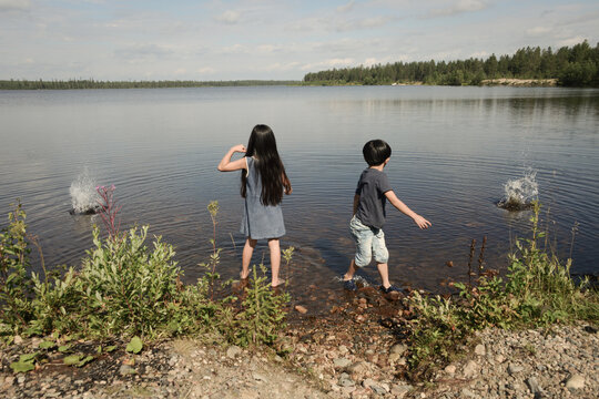 Young girl and boy playing and throwing rocks in lake in summer with a splash in Norway