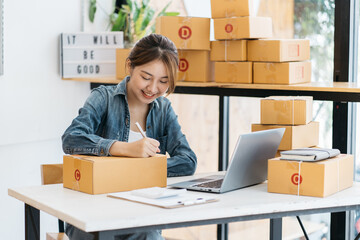 Asian woman entrepreneur is packing product to the box at home workplace. teenager business owner work at home, many stuff to do today in home. Start up SME concept.