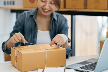Asian woman entrepreneur is packing product to the box at home workplace. teenager business owner...