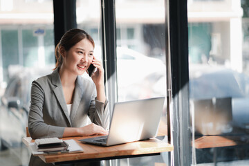Portrait of young asian business woman talk on smartphone write notebook laptop in home office....