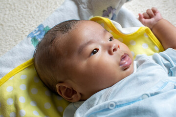 A Japanese Asian infant baby lying down on the white carpet looks at his mother with blue clothes