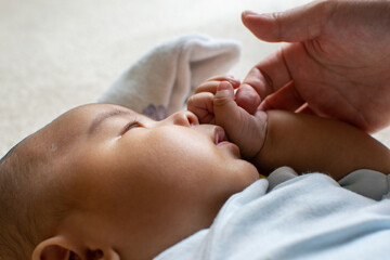 A Japanese Asian infant baby with blue clothes holds his mother's finger