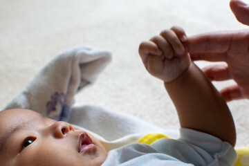 A Japanese Asian infant baby with blue clothes holds his mother's finger