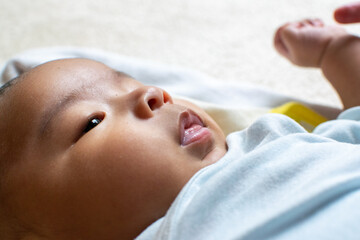 A Japanese Asian infant baby lying down on the white carpet looks at his mother with blue clothes