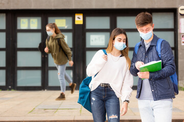Two students in protective masks discussing homework on the street