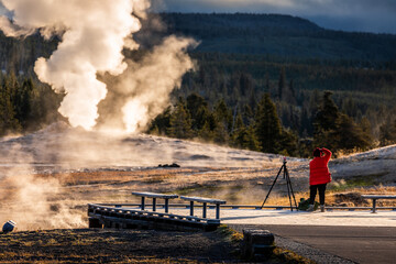 Tourist taking the explosion of old Faithful, Yellowstone in morning.