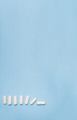Vertical banner white tablets or capsules lie on a light blue background and gradually fall with space for text. Useless pharmaceutical, Covid-19 or coronavirus