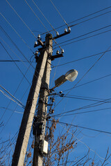 Electric wires hanging on a pole with a lighting lamp photographed from below on a background of...