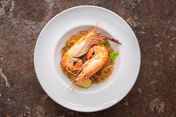 baked prawns with vermicelli, casseroled shrimps with glass noodles in white simply ceramic plate on rusty texture background, top view, flat lay, river prawn