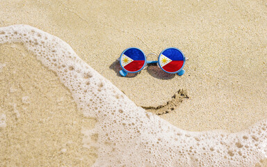 Sunglasses with flag of Philippines on a sandy beach. Nearby is a sea lightning and a painted...