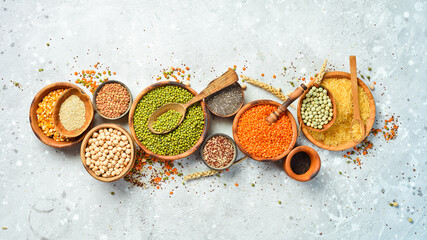 bowls of legumes, lentils, chickpeas, beans, rice and cereals on a stone background, top view.