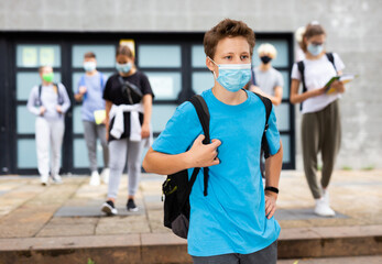 Portrait of teen student in face mask with rucksack on his way to college in warm autumn day. Back to school after lockdown concept.