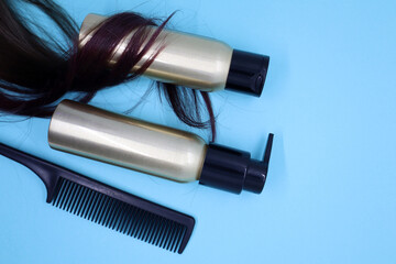 Lock of female light brown hair, hair care products on blue background.