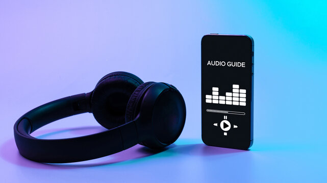 Audio guide online app on digital mobile smartphone screen with music headphones on neon background. Devices for listening audioguide to excursions.