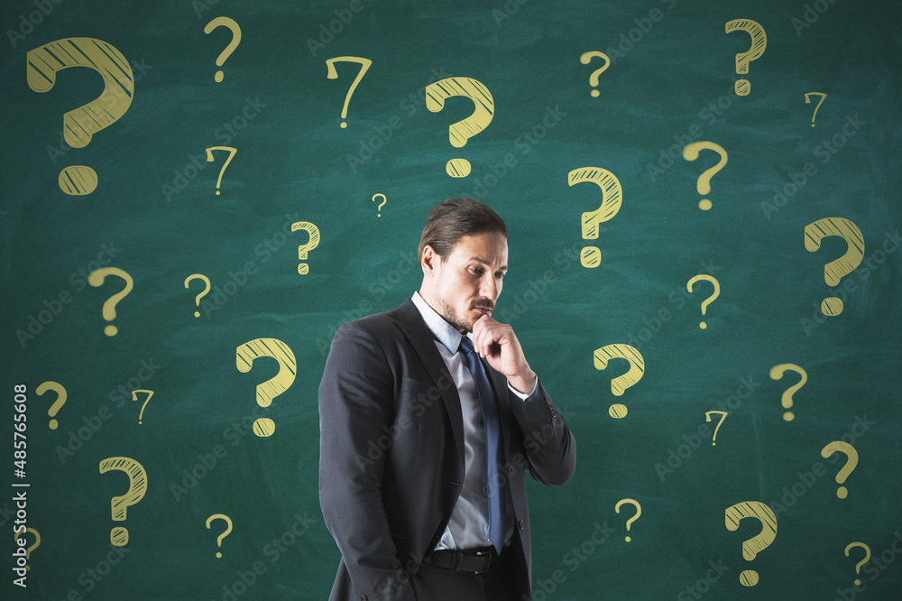 Poster Portrait of attractive thoughtful young european man on chalkboard wall background with question marks sketch. Solution and doubt concept.