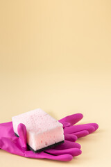 Pink dishwashing sponge and rubber gloves on neutral beige background, cleaning concept