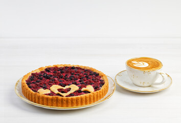 Homemade open pie with red and black raspberries and cup of coffee cappuccino on white wooden table. Copyspace.