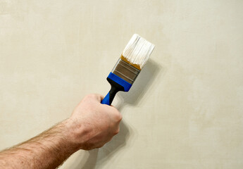 a man hand holds a brush in white paint on the background of  the wall