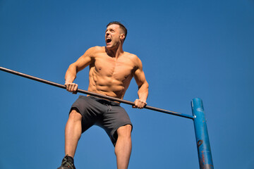 Muscular man working out in an outdoor gym, doing pull-ups.