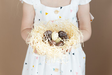 A nest with chocolate eggs in the hands of a girl. Easter concept.