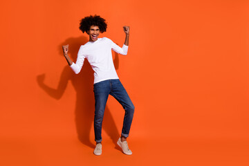 Fototapeta na wymiar Photo of excited lucky guy wear white shirt rising fists empty space isolated orange color background