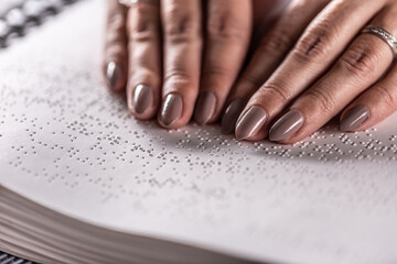 Detail of female hands of a blind reader, touching the book made in braille alphabet