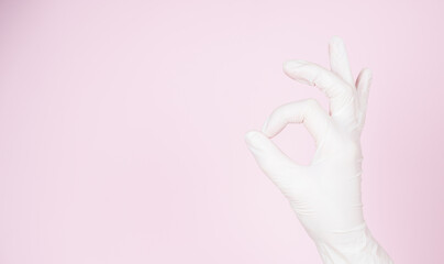 Female hand in disposable glove shows OK, isolated on pink background with copy space