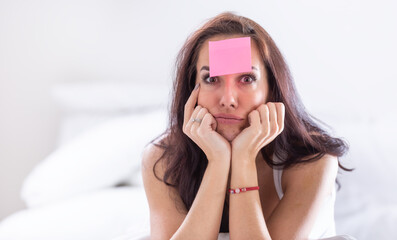 Woman who forgot something has pink postit on her forehead holding her head with both heads,...