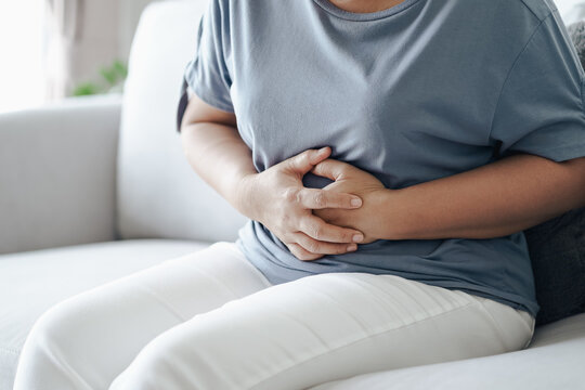 Woman suffering from stomachache sitting on the sofa at home. abdominal pain, Gastritis, Period, menstruation..