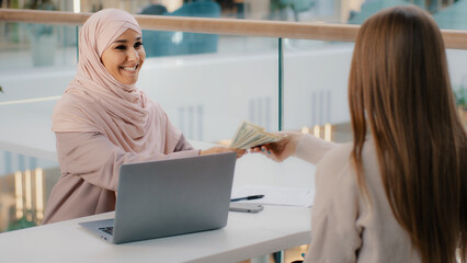 Young friendly smiling arab woman manager sits in office at desk communicates with client explains...