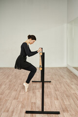 a ballerina in pointe shoes on her toes gets up from a squat at a ballet barre and holds on to it with her hands in front of a mirror