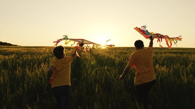 Son and dad play with kites on green field against sunset