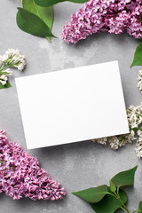 Greeting or invitation card mockup with purple and white lilac flowers branches on grey background