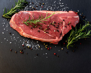 Raw beef steak with spices and rosemary on a dark background. Top view with copy space.