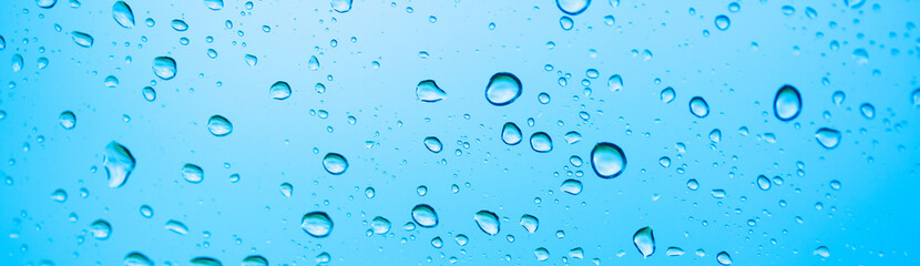 Rain outside the window. Water droplets on a car glass on a background of blue sky and green grass. Overcast. Wet clean nature, ecology