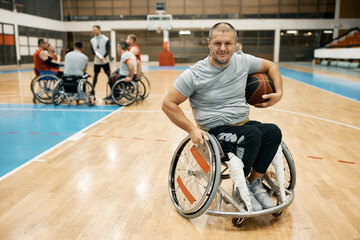 Happy wheelchair-bound basketball player with his team and coach in the background.