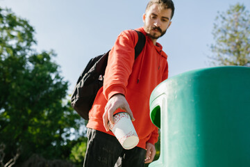 Recycling bin, closeup young man hand throwing empty paper coffee cup in the recycling bin. Eco-friendly approach concept. Keep streets, city, earth clean.